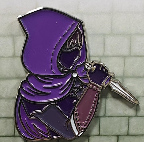 Soft enamel pin of a stealthy Rogue, dressed in a dark purple hooded robe with a mask and gloves, holding a white dagger.