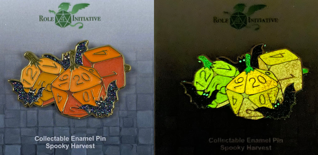 Soft enamel pin showing 3 pumpkins carved in different dice shapes: a d20, d12 and d6. These are in varying shades of orange with gold numbers. Three glittery black bats with white eyes surround the pumpkin dice. The pumpkins glow in the dark, as do the eerie bats' eyes.